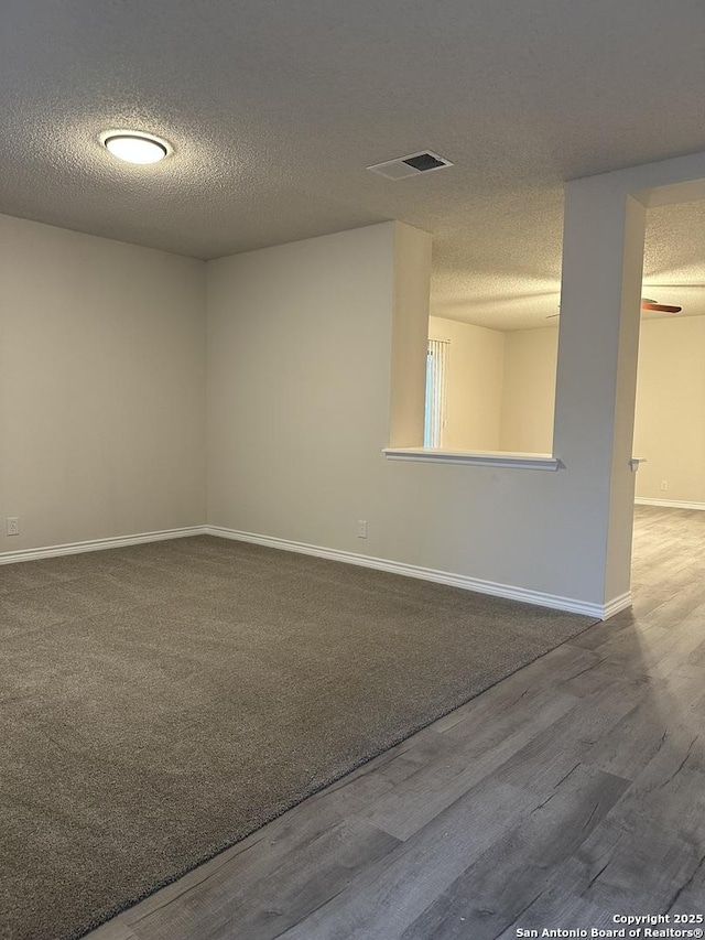 empty room with a textured ceiling, wood finished floors, visible vents, and baseboards