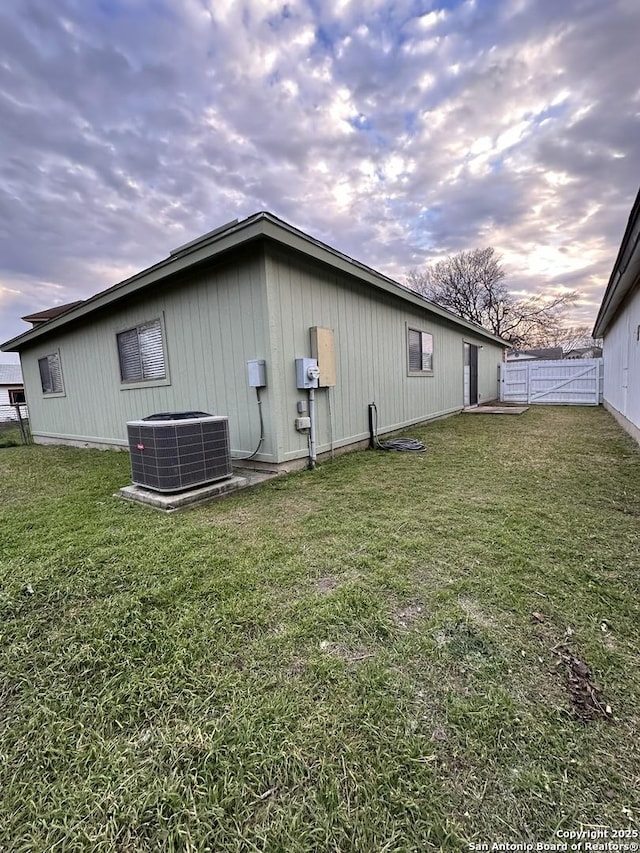 view of property exterior featuring fence, central AC unit, and a lawn