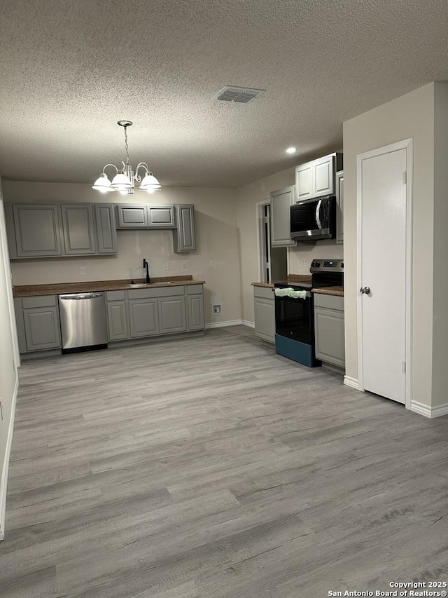 kitchen with gray cabinetry, a notable chandelier, a sink, appliances with stainless steel finishes, and light wood-type flooring