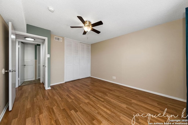 unfurnished bedroom with a textured ceiling, wood finished floors, visible vents, baseboards, and a closet