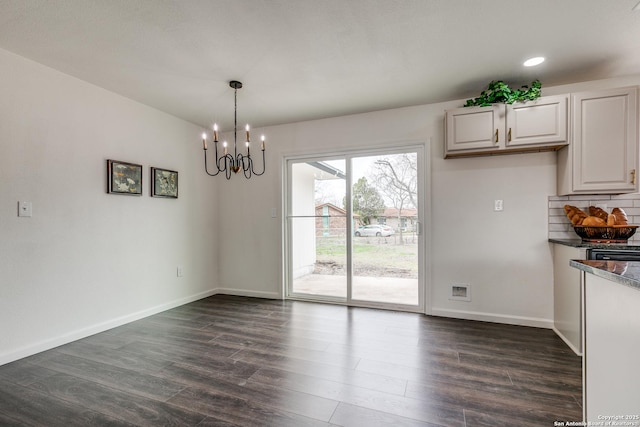 unfurnished dining area with dark wood finished floors, a notable chandelier, and baseboards