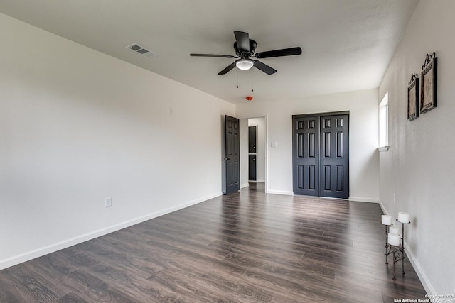 spare room with ceiling fan, visible vents, baseboards, and dark wood finished floors