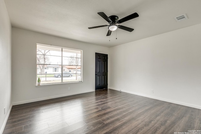 unfurnished room with dark wood-type flooring, a ceiling fan, visible vents, and baseboards