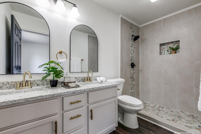 full bath featuring toilet, double vanity, tiled shower, wood finished floors, and a sink