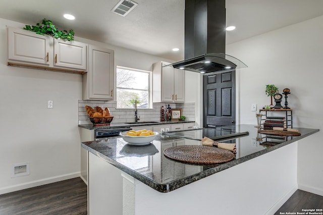 kitchen featuring visible vents, island exhaust hood, a sink, backsplash, and dark wood-style floors
