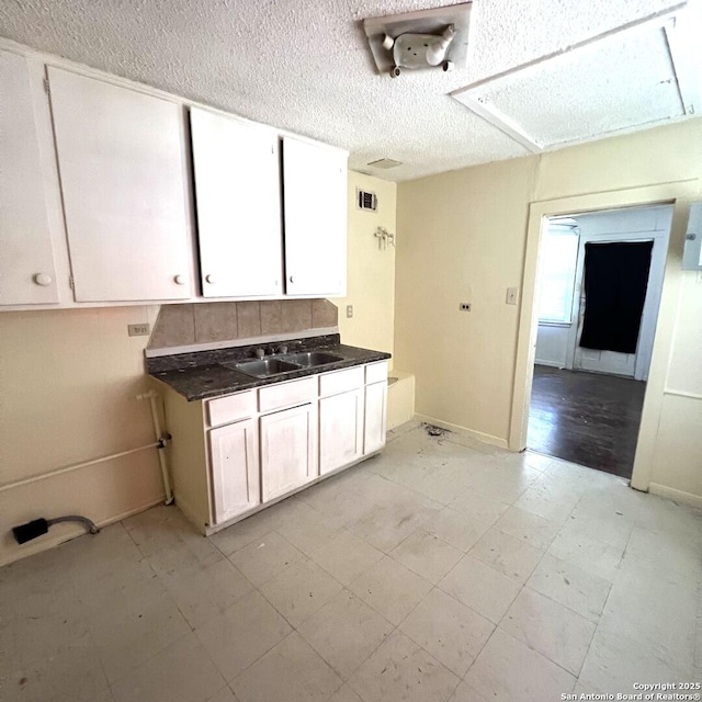 kitchen featuring dark countertops, visible vents, white cabinetry, a sink, and a textured ceiling