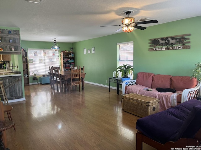 living area with visible vents, a ceiling fan, a textured ceiling, wood finished floors, and baseboards