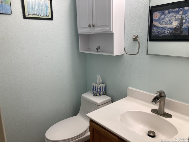 half bathroom featuring a textured wall, vanity, and toilet