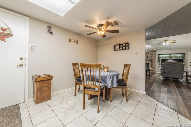 dining space with light tile patterned floors, visible vents, baseboards, ceiling fan, and a brick fireplace