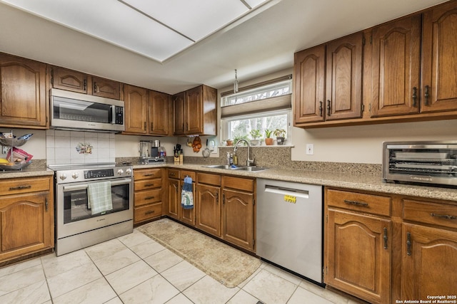 kitchen with light countertops, appliances with stainless steel finishes, brown cabinetry, and a sink