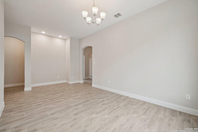 unfurnished room featuring arched walkways, a notable chandelier, visible vents, baseboards, and light wood-type flooring