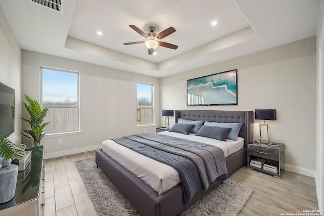 bedroom featuring light wood-type flooring, baseboards, visible vents, and a raised ceiling