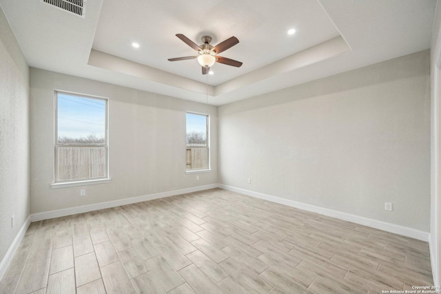 empty room with ceiling fan, visible vents, baseboards, light wood-style floors, and a tray ceiling