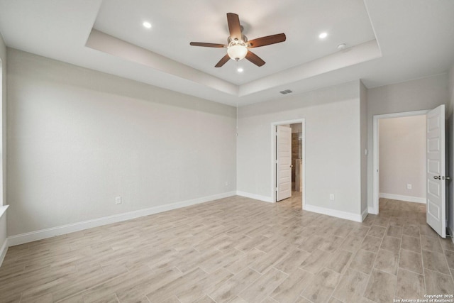 unfurnished bedroom featuring a tray ceiling, baseboards, visible vents, and light wood finished floors