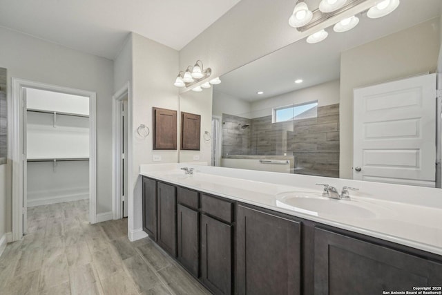 bathroom with a walk in closet, double vanity, a sink, wood finished floors, and walk in shower