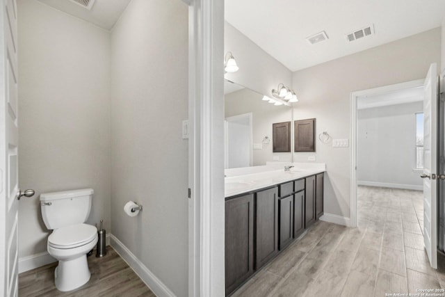 full bathroom featuring toilet, double vanity, visible vents, and wood finished floors