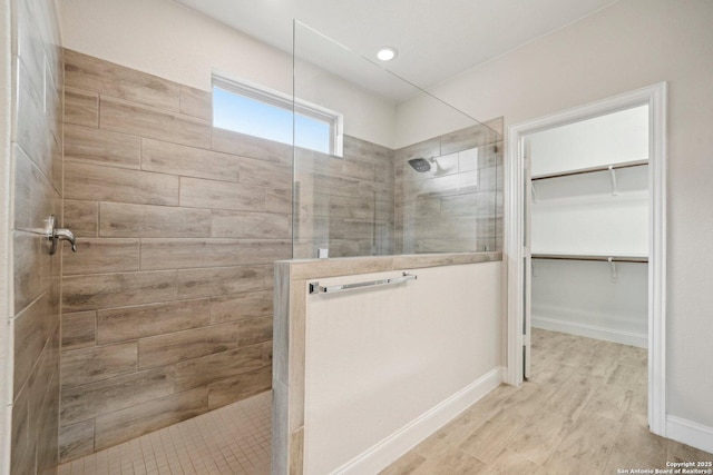 bathroom with a spacious closet, wood finished floors, walk in shower, and baseboards