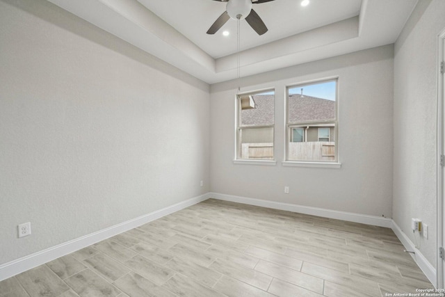 spare room featuring a tray ceiling, ceiling fan, light wood-style flooring, and baseboards