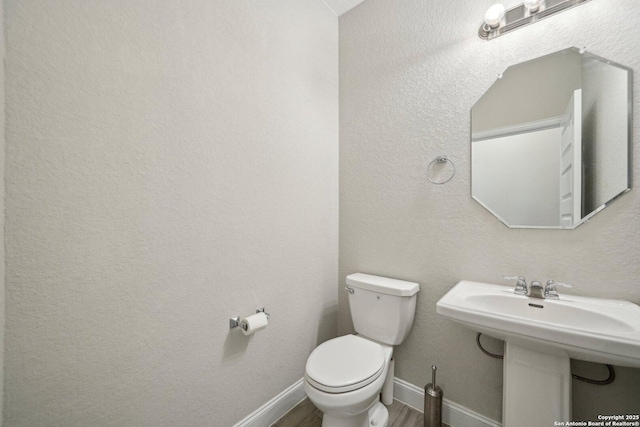 half bathroom with toilet, baseboards, a sink, and wood finished floors