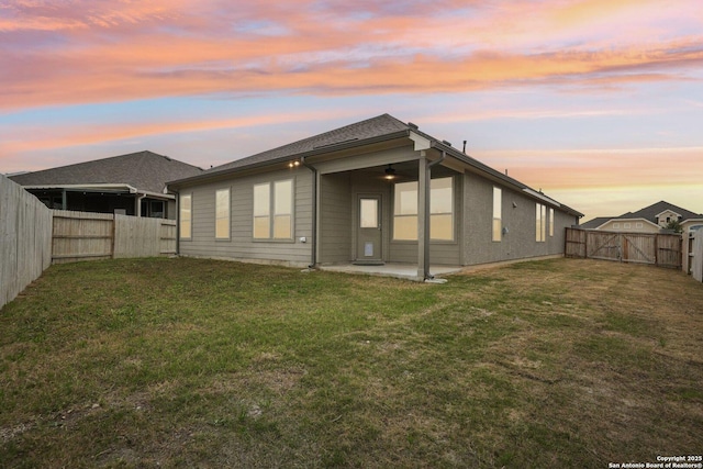 back of house at dusk with a patio area, a fenced backyard, a gate, and a lawn