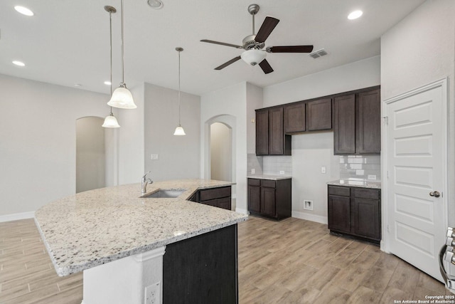 kitchen featuring visible vents, arched walkways, light wood-style flooring, a sink, and backsplash