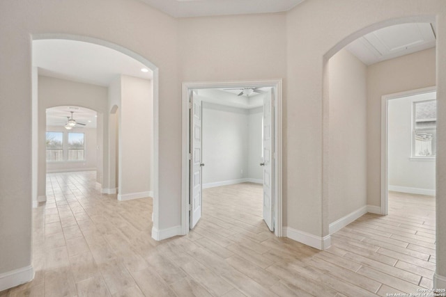 hallway featuring arched walkways, baseboards, and light wood finished floors