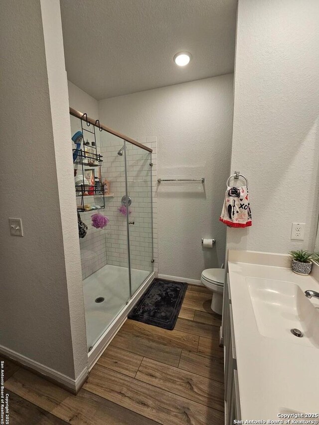106 Tokalaun Dr, Hutto, TX 78634 - full bathroom featuring baseboards, toilet, wood finished floors, a textured ceiling, and a shower stall