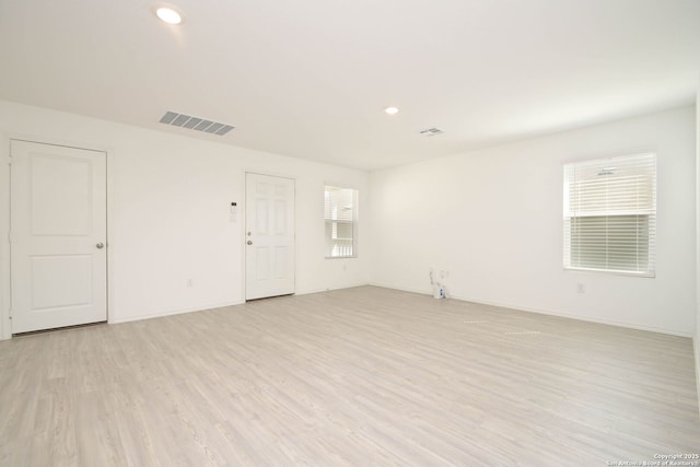 spare room featuring a wealth of natural light, light wood-type flooring, visible vents, and baseboards