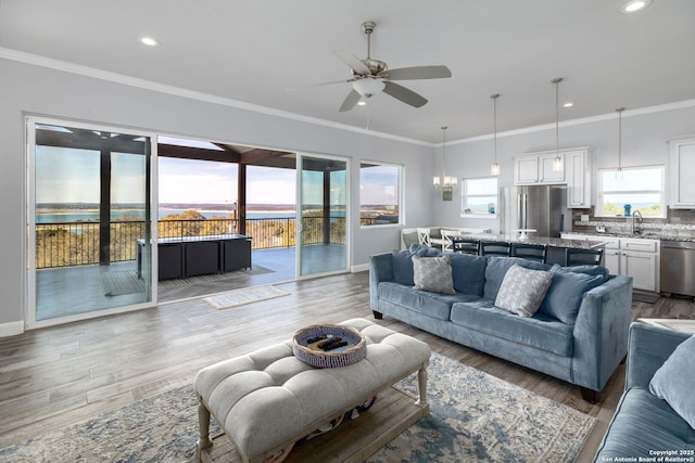 living room featuring light wood-type flooring, crown molding, recessed lighting, and ceiling fan with notable chandelier