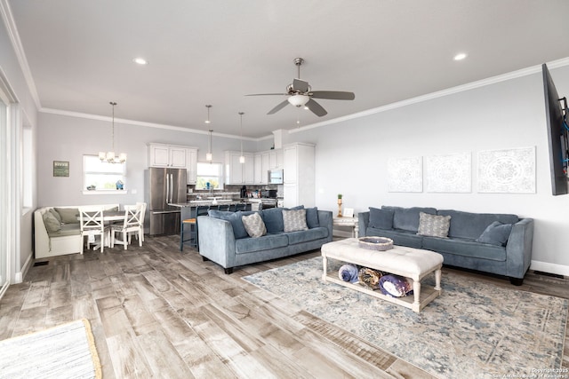 living room featuring light wood-style floors, baseboards, crown molding, and ceiling fan with notable chandelier