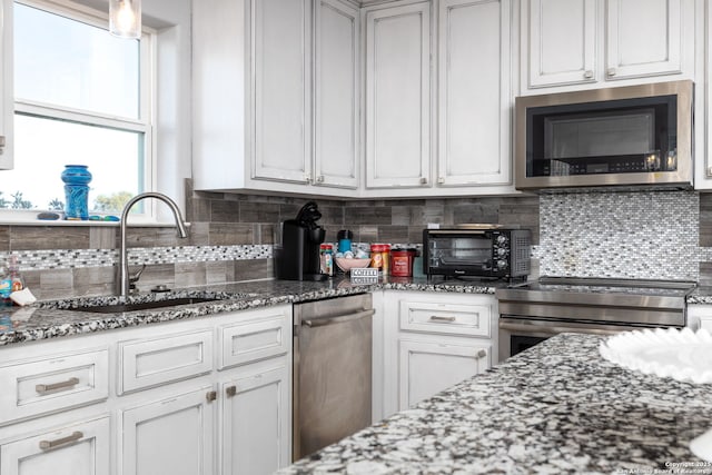 kitchen with dark stone counters, appliances with stainless steel finishes, backsplash, and a sink