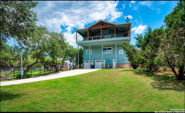 back of house featuring a balcony, a yard, stone siding, concrete driveway, and a chimney