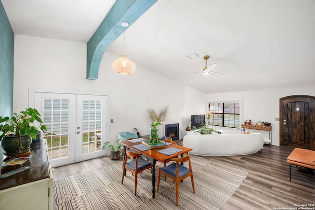 living area featuring french doors, vaulted ceiling with beams, a lit fireplace, and wood finished floors