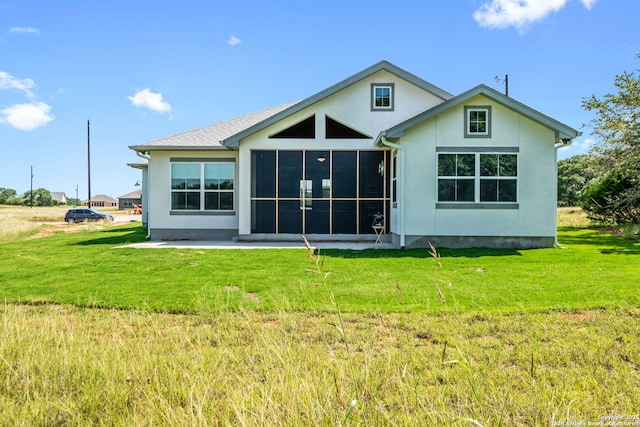 rear view of property featuring a sunroom, a lawn, and stucco siding