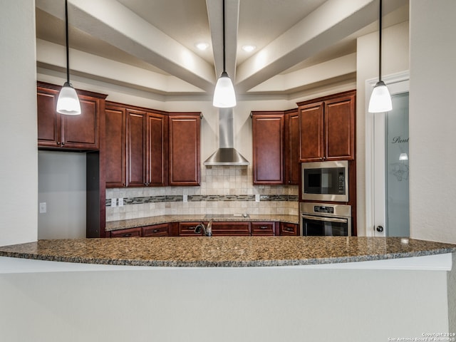 kitchen featuring decorative backsplash, a raised ceiling, appliances with stainless steel finishes, hanging light fixtures, and wall chimney range hood