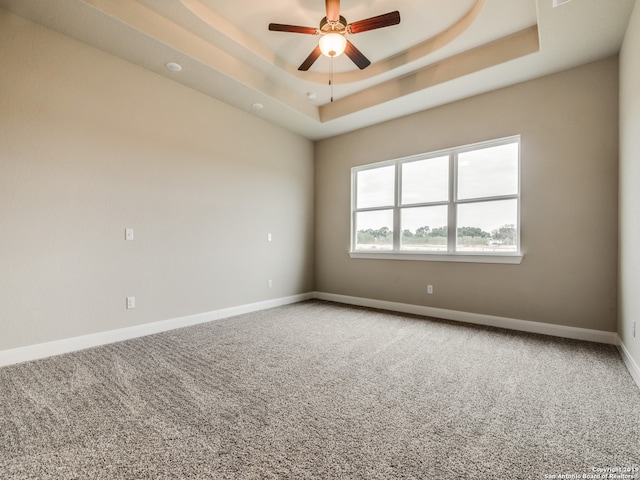 carpeted empty room featuring a ceiling fan, a raised ceiling, and baseboards