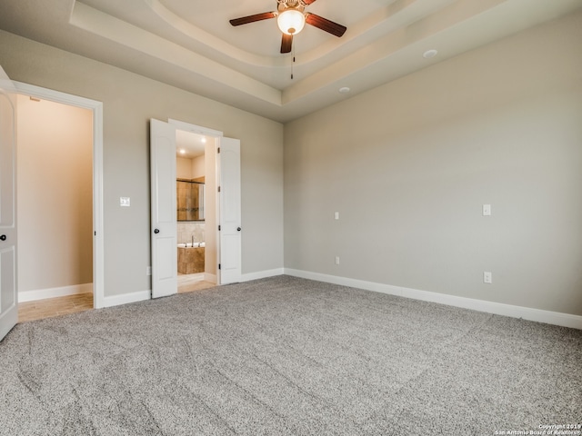 unfurnished bedroom featuring light carpet, baseboards, a raised ceiling, and connected bathroom