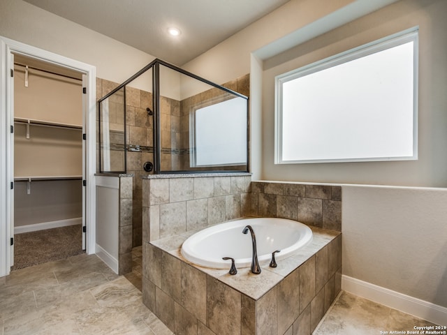 bathroom with a garden tub, a stall shower, a walk in closet, and baseboards