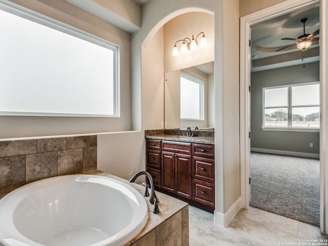 bathroom with ceiling fan, vanity, a bath, and baseboards