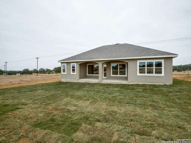 back of property featuring roof with shingles, a yard, and stucco siding