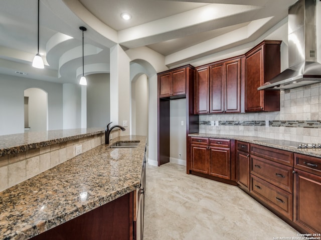 kitchen featuring light stone counters, black electric stovetop, a raised ceiling, a sink, and wall chimney exhaust hood