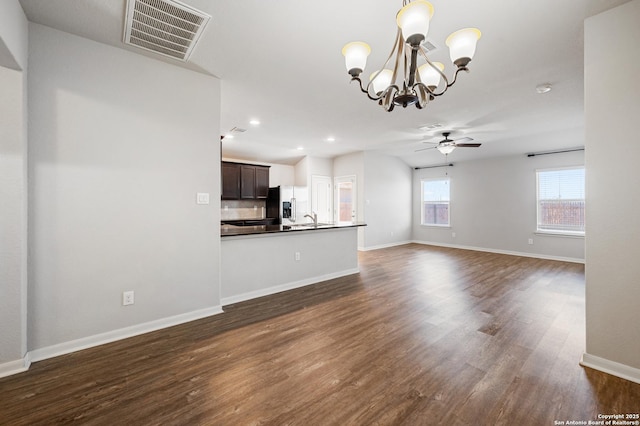 unfurnished living room with dark wood-style flooring, visible vents, a sink, baseboards, and ceiling fan with notable chandelier