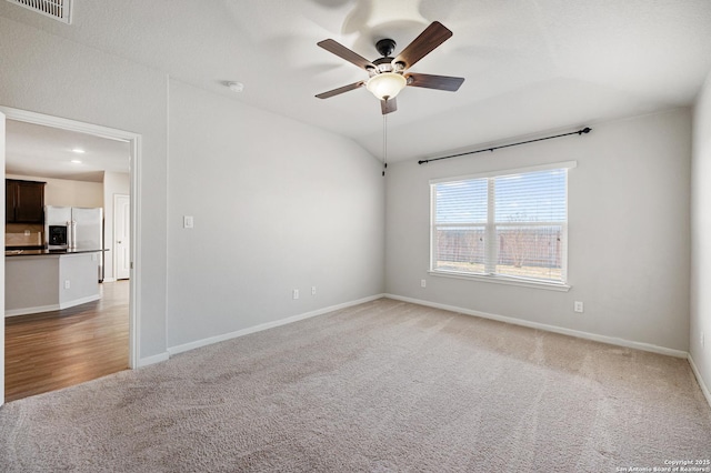 empty room featuring light colored carpet, visible vents, vaulted ceiling, ceiling fan, and baseboards