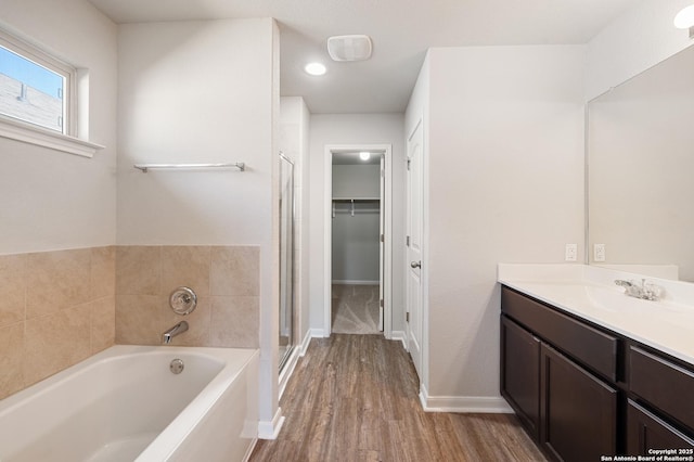 bathroom featuring a garden tub, a spacious closet, a stall shower, vanity, and wood finished floors