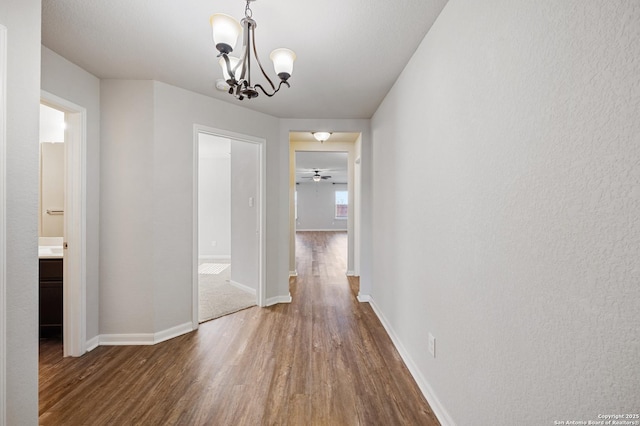 corridor featuring a notable chandelier, baseboards, and wood finished floors