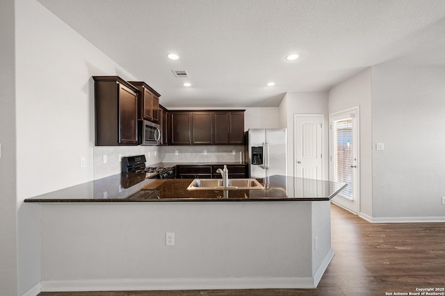 kitchen with dark brown cabinetry, visible vents, a peninsula, stainless steel appliances, and a sink