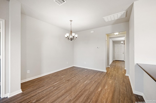 empty room featuring wood finished floors, visible vents, baseboards, and an inviting chandelier