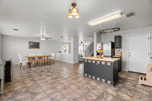 kitchen with a ceiling fan, freestanding refrigerator, visible vents, and dark cabinetry