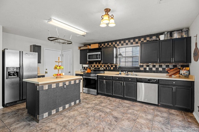 kitchen with dark cabinets, stainless steel appliances, a sink, light countertops, and tasteful backsplash