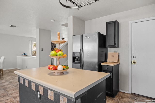 kitchen with a kitchen island, visible vents, light countertops, dark cabinetry, and stainless steel fridge